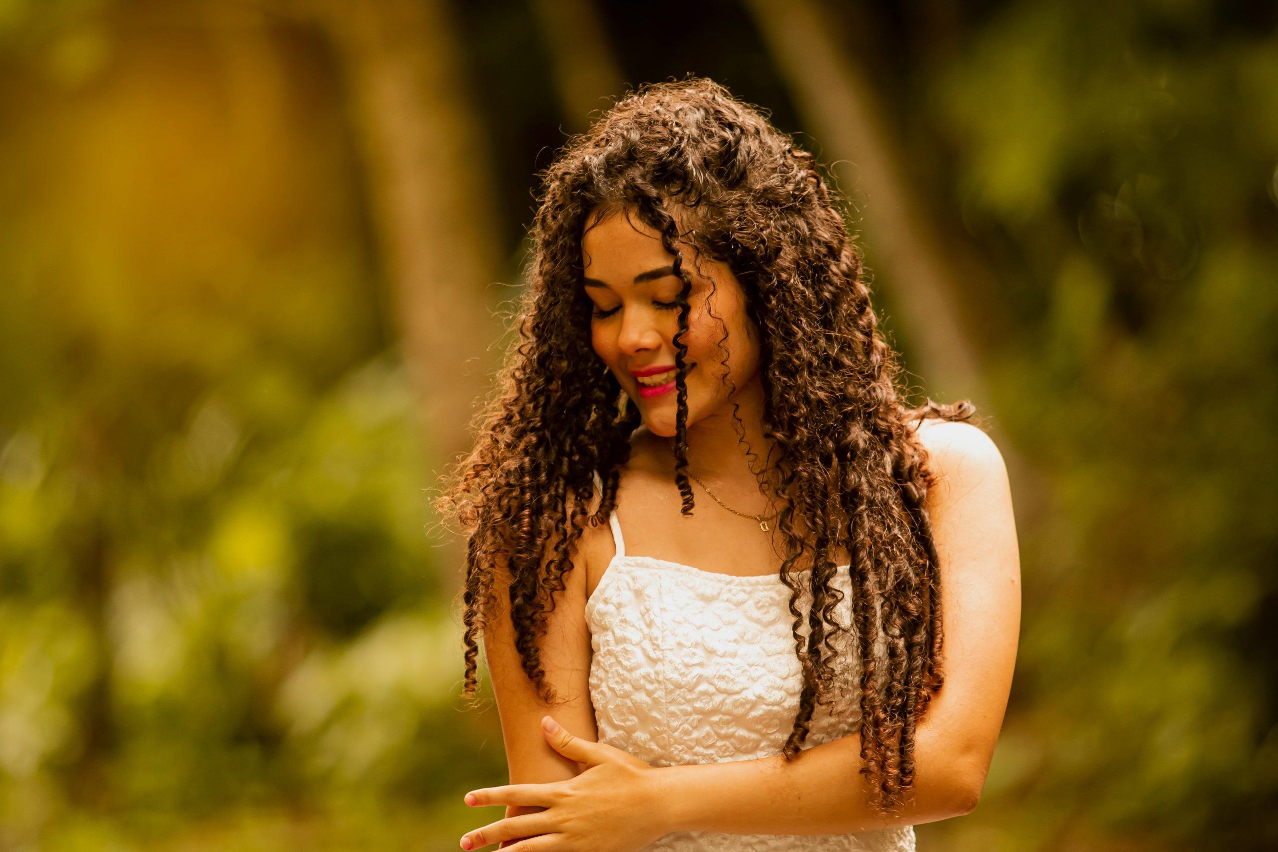 Portrait of a smiling woman with curly hair in a white dress, enjoying nature.