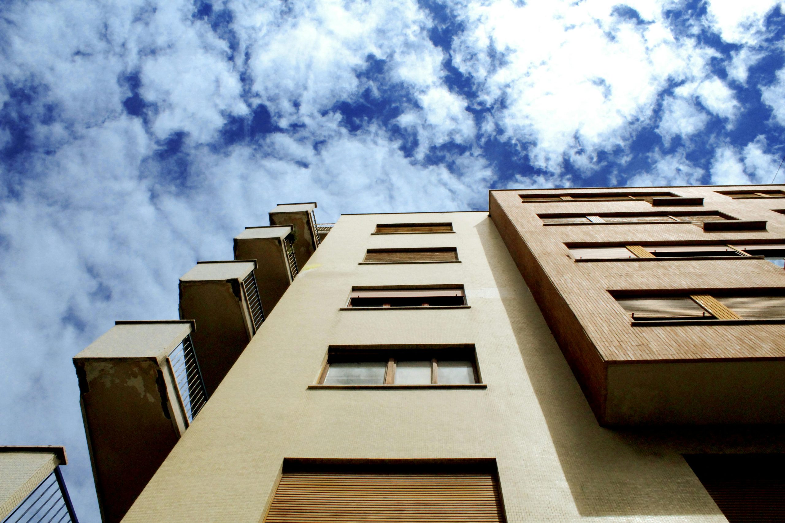 Low-angle shot of a modern building facade against a vibrant blue sky with clouds.