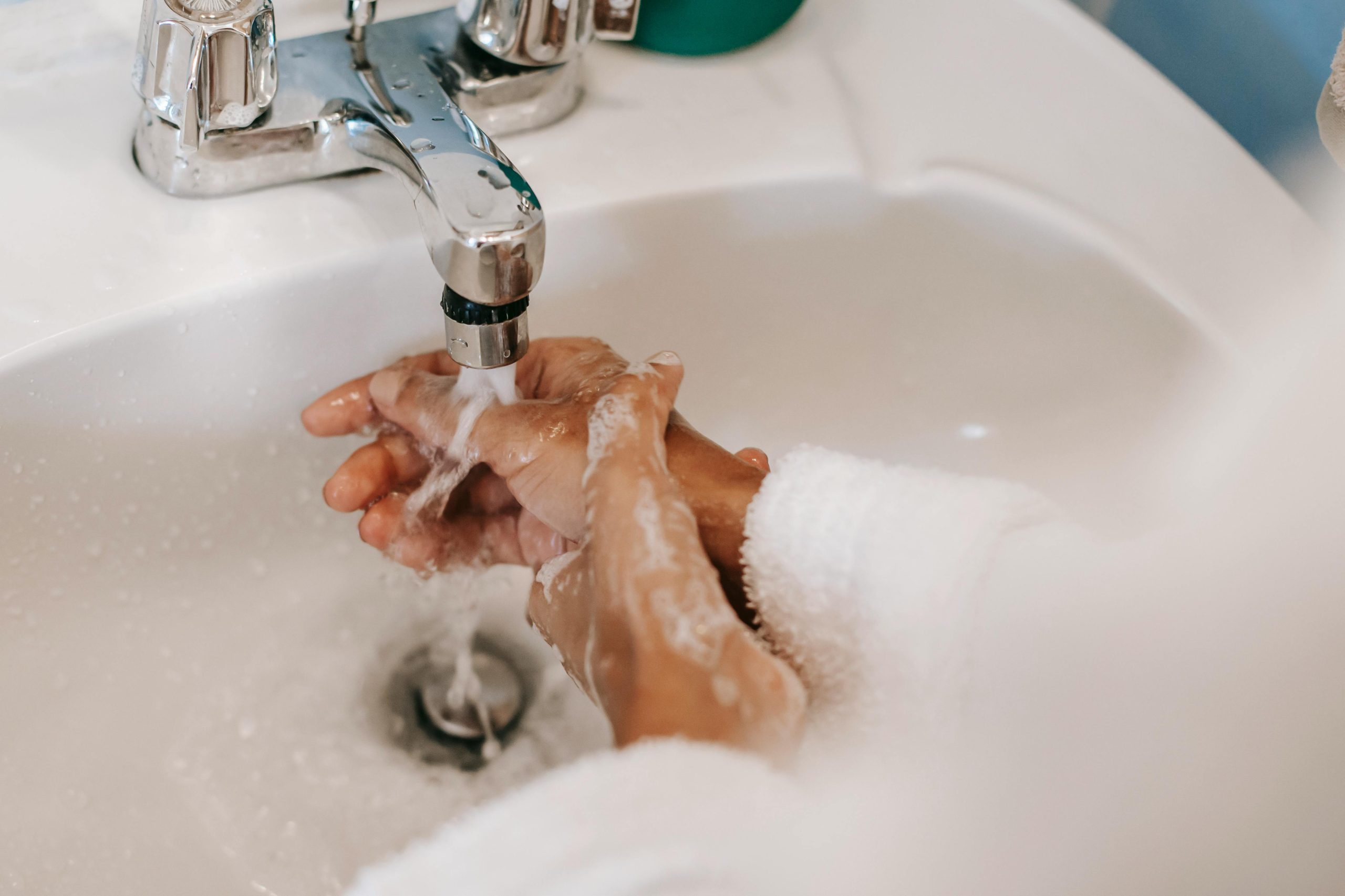 High angle of crop anonymous ethnic female washing hands with foamy water during morning hygiene routine