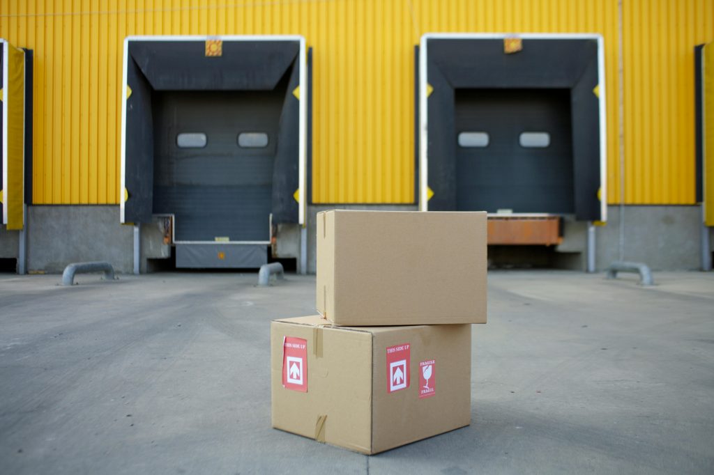 Cardboard boxes stacked in front of industrial warehouse loading docks with yellow walls.