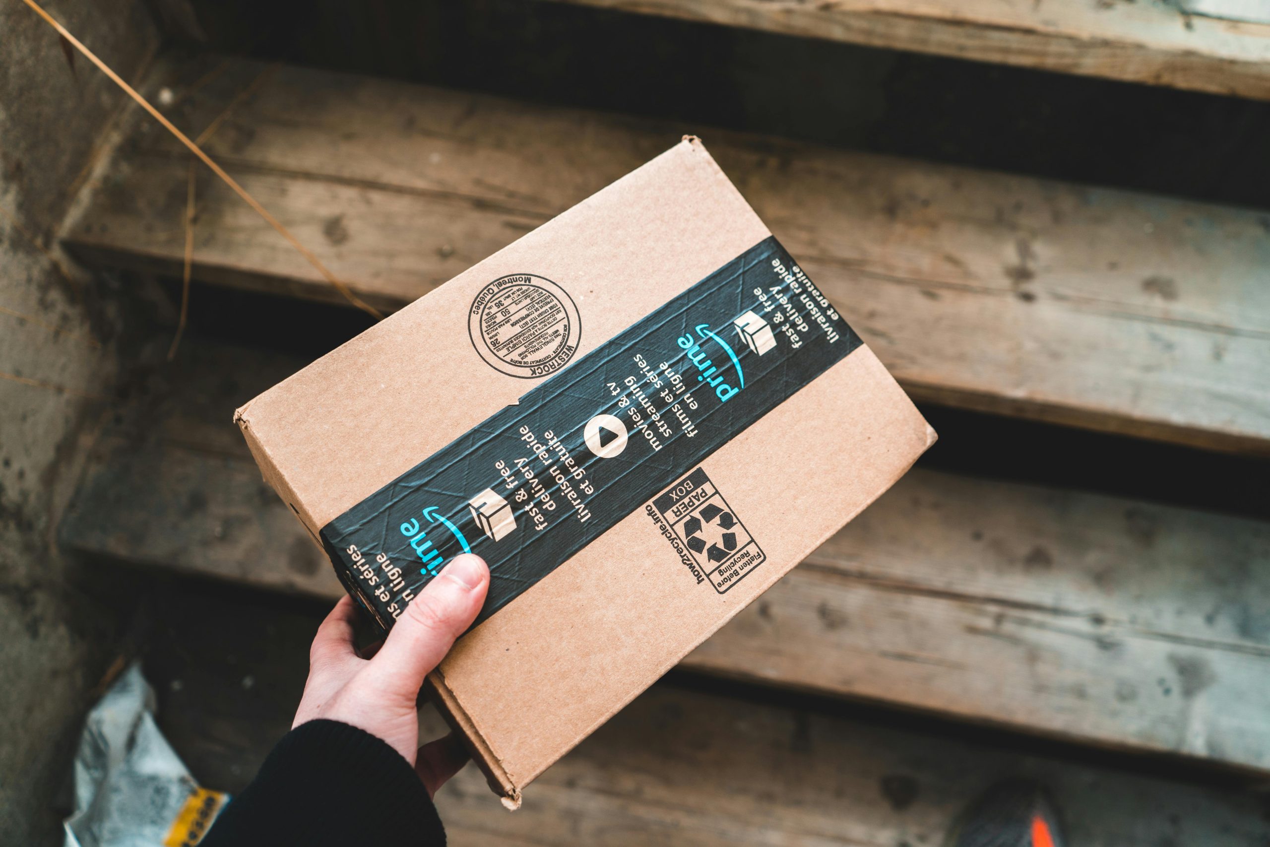 A close-up of a person's hand holding a cardboard package on wooden stairs.