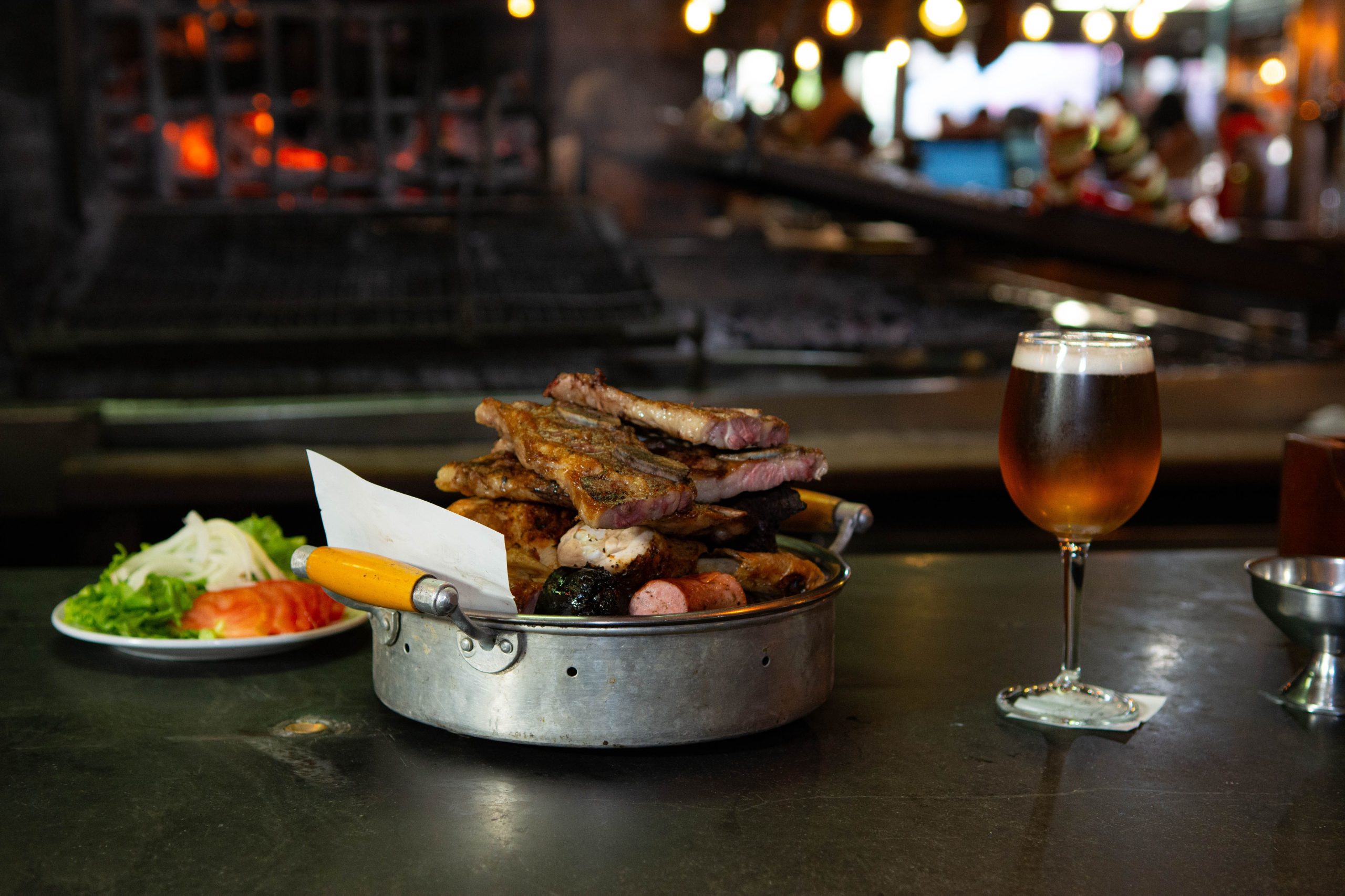 An indoor setting showcasing a BBQ platter with assorted meats and a refreshing glass of beer.