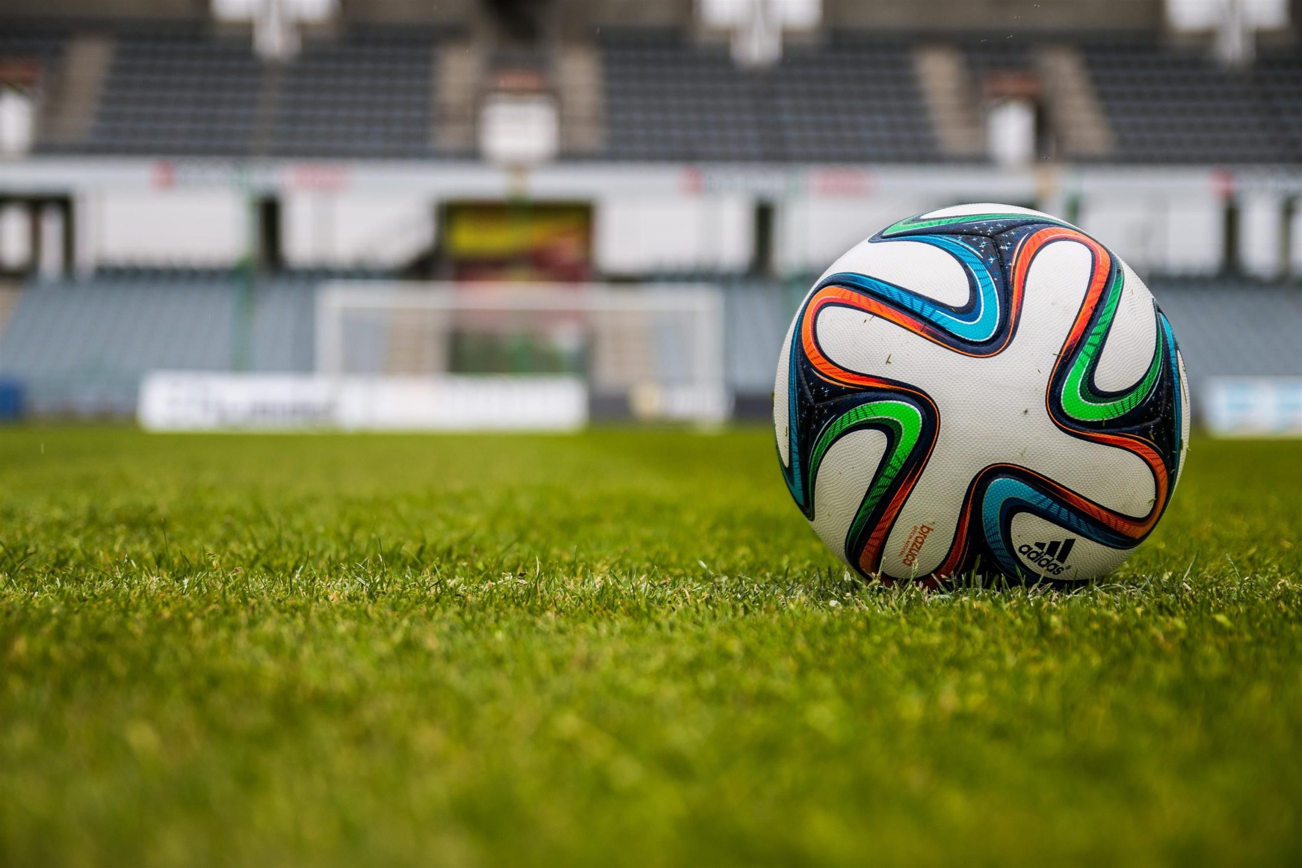 Vibrant soccer ball on a lush green field in an empty stadium.