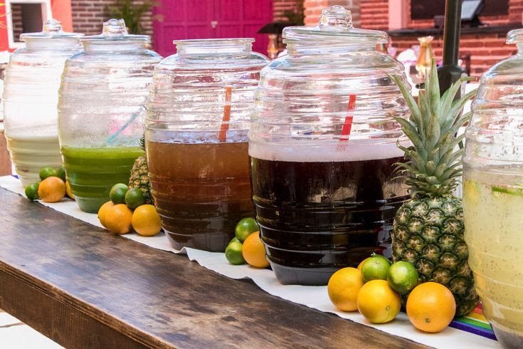 Jarras y vasos tradicionales con aguas frescas de frutas naturales en mesa festiva mexicana