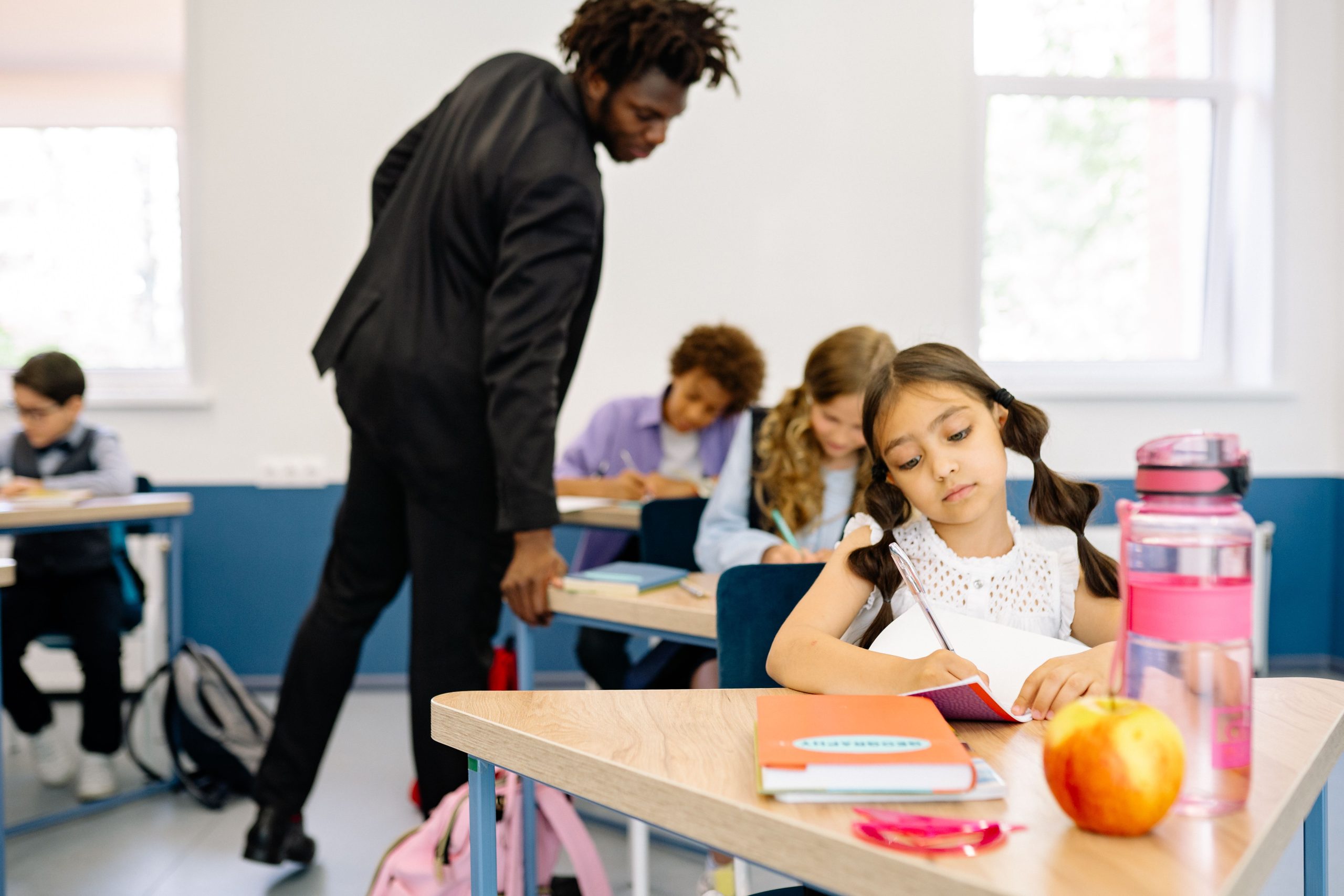 Educación y salud mental infantil: 8 de cada 10 docentes advierten mayores dificultades en el manejo de la frustración escolar A classroom scene with children studying while a teacher provides guidance, fostering learning.
